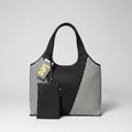 A Lee brand tote bag with a black and white striped woven body, black leather trim, and a black zippered pouch attached, resting on a textured surface with plastic bags in the background.