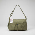 An olive green nylon shoulder bag with a drawstring closure and a hanging tag, sitting on a patterned stool surrounded by cluttered plastic bags and other items.