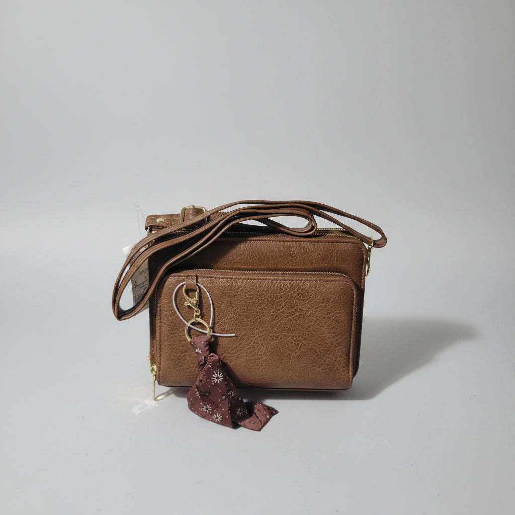 A brown pebbled leather crossbody bag with a gold-tone clasp and a small burgundy scarf accent, shown on a white surface with a blue tag attached.