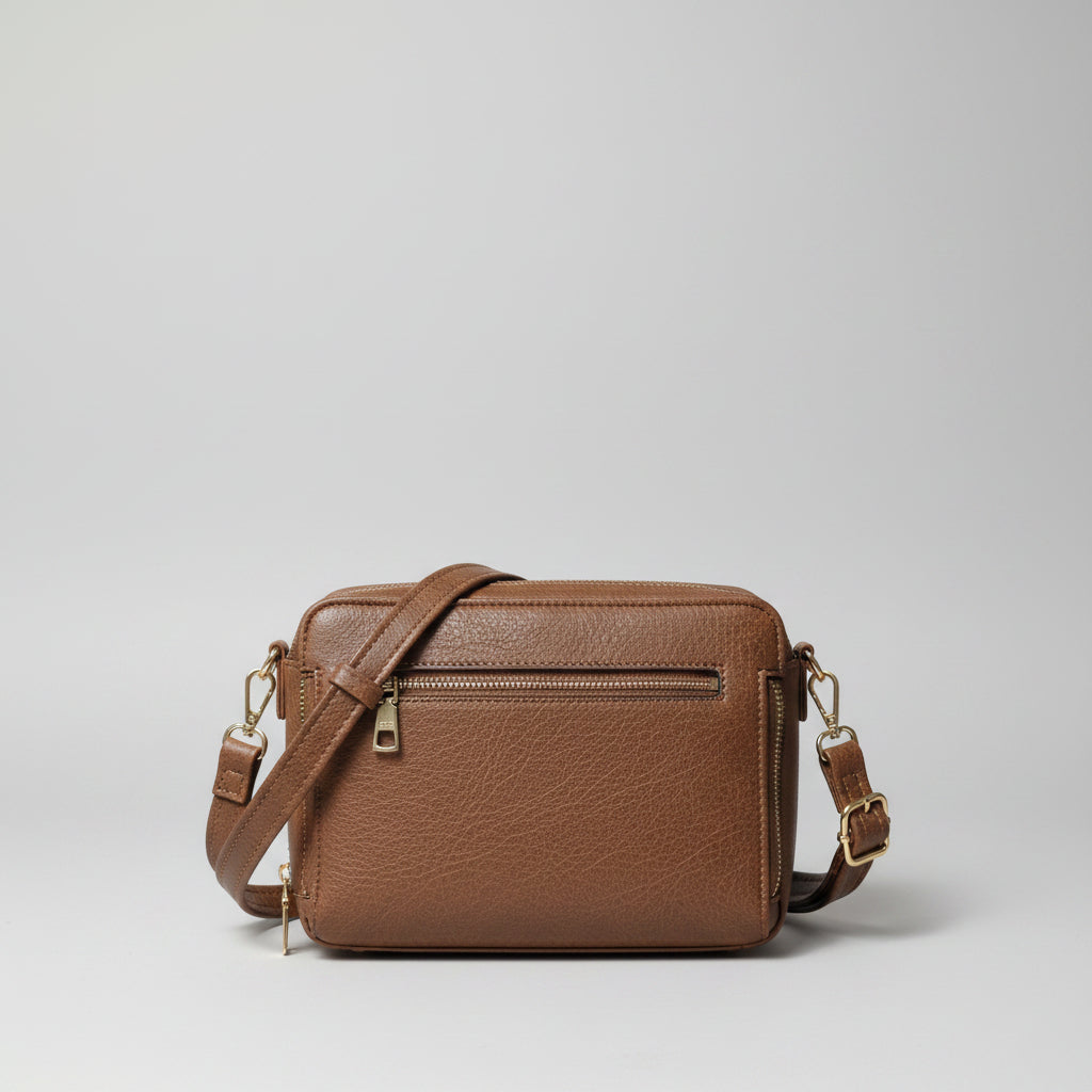 A brown faux-leather crossbody bag with gold-tone hardware, shown with its straps and a blue circular tag on a white surface.