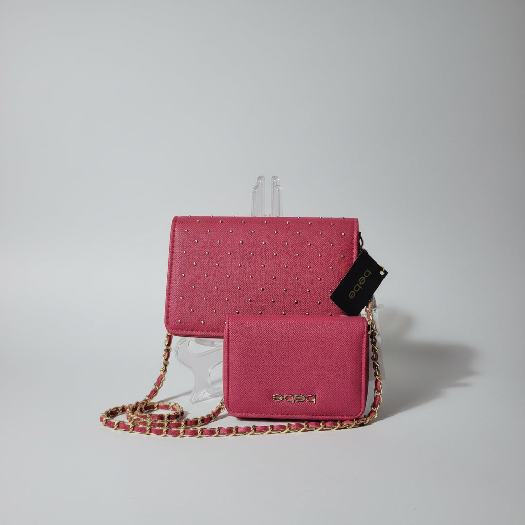 A pink textured crossbody bag with gold studs and a matching small pouch, displayed on a white surface with a clear stand. The brand name 'beqa' is visible on the black hangtag and the front of the pouch.
