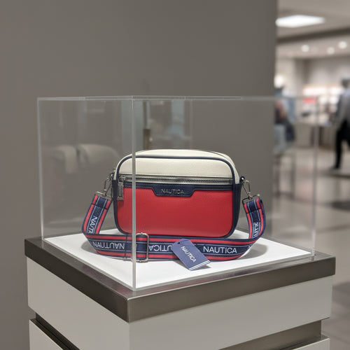 A Nautica crossbody bag with a red and cream pebbled leather body and a navy blue webbed strap featuring the brand name in white. The bag is shown with its retail hangtag on a white surface.