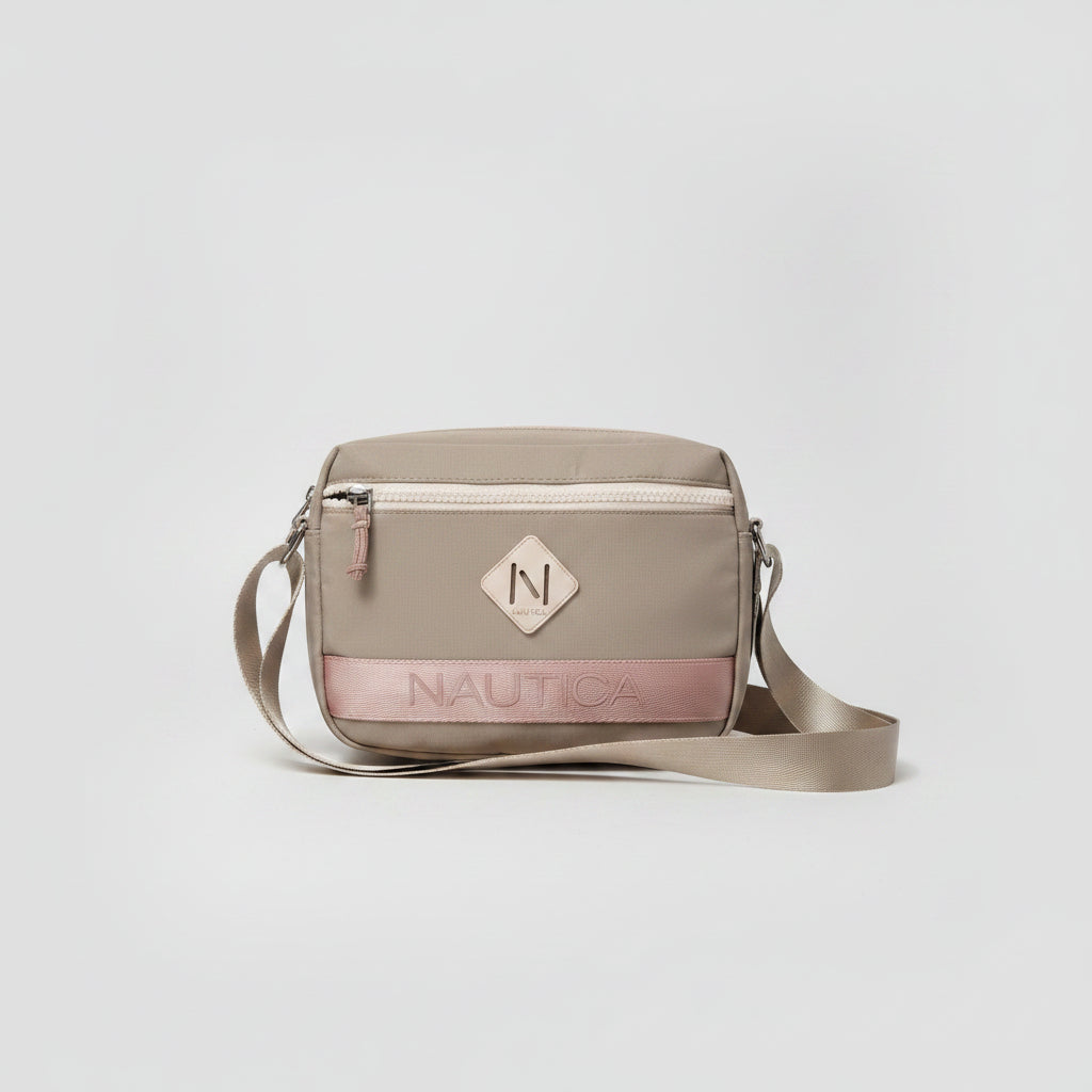A beige Nautica crossbody bag with a pink stripe and a diamond-shaped logo patch, displayed on a clear stand on a white sheet of paper.