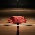 A coral red canvas fanny pack with a black Jumpman logo patch on the front, resting on a white surface with a patterned mat underneath.